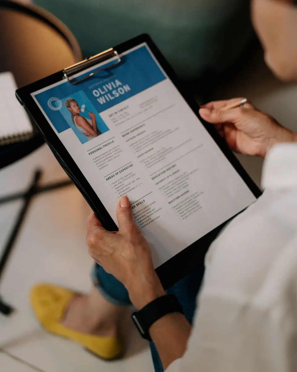 A recruiter holding a printed CV on a clipboard, pen in hand.